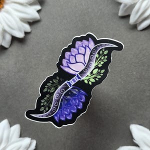 May include: A sticker featuring a stylized design of a lotus flower and a curved blade. The lotus is depicted in shades of purple and the blade has a decorative pattern. Green leaves and a black border complete the design.