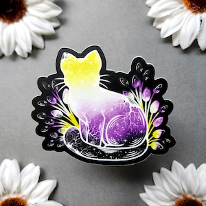 May include: A sticker featuring a cat design with non-binary pride colors. The cat is yellow, white, and purple with a galaxy pattern. The sticker is surrounded by black leaves and purple and yellow accents.