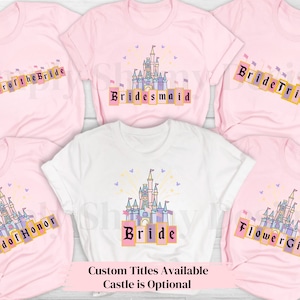 Puede incluir: Cinco camisetas rosas con diferentes textos y una camiseta blanca con la palabra "Bride" en ella. Cada camiseta presenta una imagen de dibujos animados de un castillo con banderas y fuegos artificiales. El texto en las camisetas dice "Mother of the Bride", "Bridesmaid", "Bride Tribe", "Maid of Honor", "Flower Girl" y "Bride".