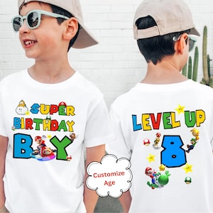 May include: Two white t-shirts with a Super Mario Bros. theme. One shirt says "Super Birthday Boy" with a picture of Mario on a kart. The other shirt says "Level Up 8" with a picture of Mario, Luigi, and Yoshi.