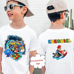 Könnte beinhalten: Weißes T-Shirt mit einem bunten Super Mario Kart-Design auf der Vorderseite und dem Namen "Ezequiel" auf der Rückseite. Das Design zeigt Mario, der ein Kart mit anderen Charakteren aus dem Spiel fährt.