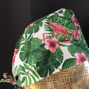 Op de afbeelding: Een witte scrub-muts met een tropische print met roze flamingo's en groene palmbladeren.