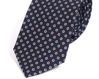 May include: A navy blue tie with a white and orange patterned design. The pattern is a small, repeating geometric shape.