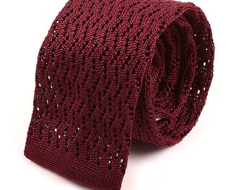 May include: A burgundy knitted tie with a textured, open weave pattern. The tie is rolled up and tied in a knot.