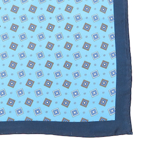 May include: A light blue pocket square with a repeating pattern of small squares in white, orange, and blue. The pocket square has a dark blue border.
