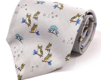 May include: A light gray necktie with a repeating pattern of owls, trees, moons, and stars. The owls are perched on blue branches. The tie has a subtle striped texture.