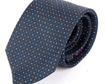 May include: A gray patterned silk tie with blue, white, and orange geometric shapes. The tie is folded and tied in a knot.