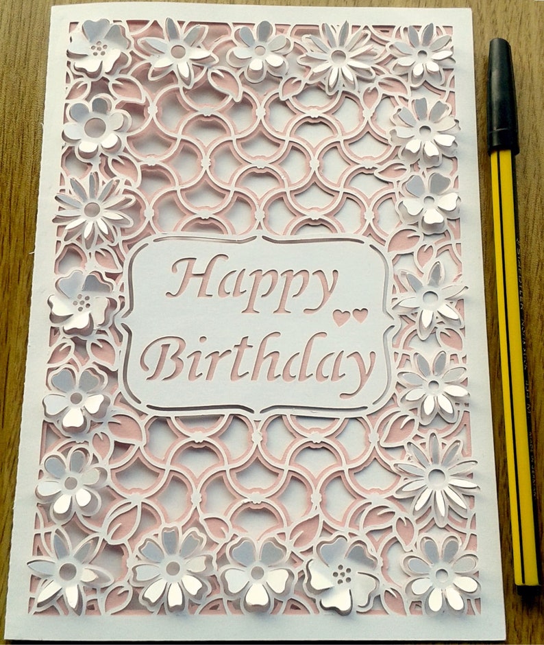 May include: A white card with a pink and white intricate design. The card has a white cutout with the text "Happy Birthday" in pink.