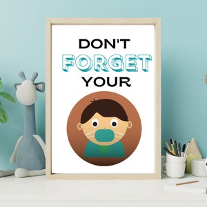 May include: A framed print with the text "DON'T FORGET YOUR" above a cartoon illustration of a person wearing a face mask. The print has a light wood frame and is displayed on a white surface with a blue wall in the background.