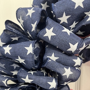 May include: Close-up of a navy blue ribbon with white stars printed on it. The ribbon is folded and twisted, creating a textured look.
