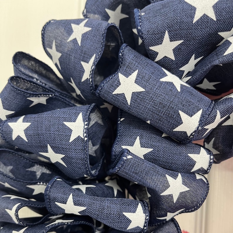 May include: Close-up of a navy blue ribbon with white stars printed on it. The ribbon is folded and twisted, creating a textured look.