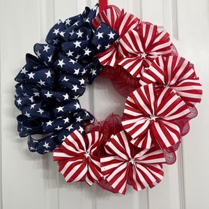 May include: A red, white, and blue patriotic wreath made of fabric and mesh. The wreath is decorated with stars and stripes.