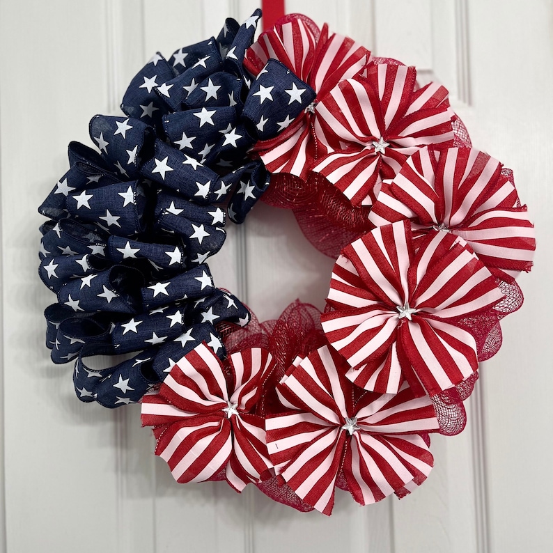May include: A red, white, and blue patriotic wreath made of fabric and mesh. The wreath is decorated with stars and stripes.