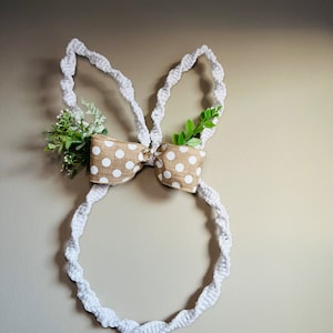 May include: A white crocheted bunny wreath with brown and white polka dot ribbon and green leaves.