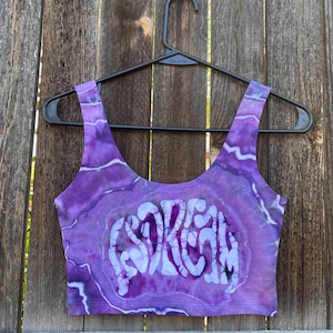 May include: Purple tie-dye crop top with the word "SORELY" printed in white on the front.