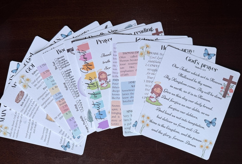 Może przedstawiać: Zbi&oacute;r białych kart z kolorowym tekstem i ilustracjami. Karty zawierają motywy religijne, w tym modlitwy, wersety biblijne i Owoc Ducha. Motyle i kwiatowe akcenty zdobią karty.