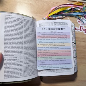 Może przedstawiać: Otwarta Biblia z zieloną okładką, wyświetlająca tekst z Księgi Wyjścia i zakładkę z dziesięcioma przykazaniami. Widoczne są kolorowe wstążki i ozdobna naklejka.