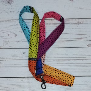 Könnte beinhalten: Ein Stoff-Lanyard mit einem mehrfarbigen Patchwork-Design und einem durchgehenden schwarzen Punktemuster. Die Stoffsegmente sind in den Farben Hellblau, Limettengrün, Pink, Lila, Orange und Gelb gehalten und mit einem drehbaren Metallhaken versehen.