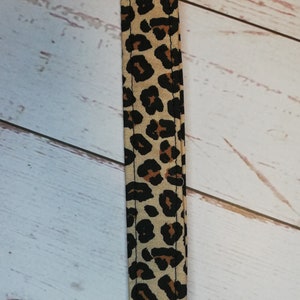 May include: A close-up of a brown and black leopard print fabric strap. The strap is sewn with a black thread.