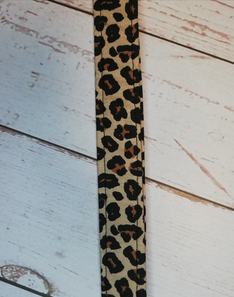 May include: A close-up of a brown and black leopard print fabric strap. The strap is sewn with a black thread.