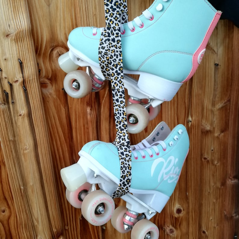 May include: A pair of light blue roller skates with white wheels and a leopard print strap. The skates have a pink accent on the side and one skate has the word "Rio" written on the side.