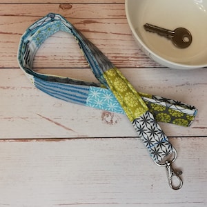 Könnte beinhalten: Ein blaues, gelbes und weißes gemustertes Stoffband mit einem silbernen Schlüsselring.