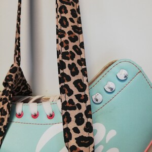 May include: A pair of light blue roller skates with white laces and a leopard print strap. The skates have silver accents and a white graphic on the side.
