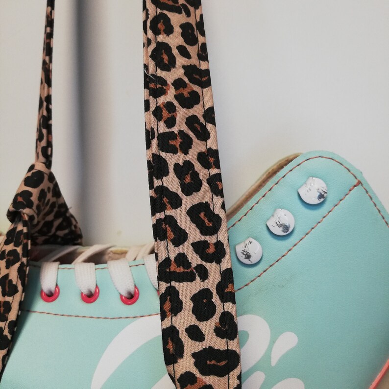 May include: A pair of light blue roller skates with white laces and a leopard print strap. The skates have silver accents and a white graphic on the side.