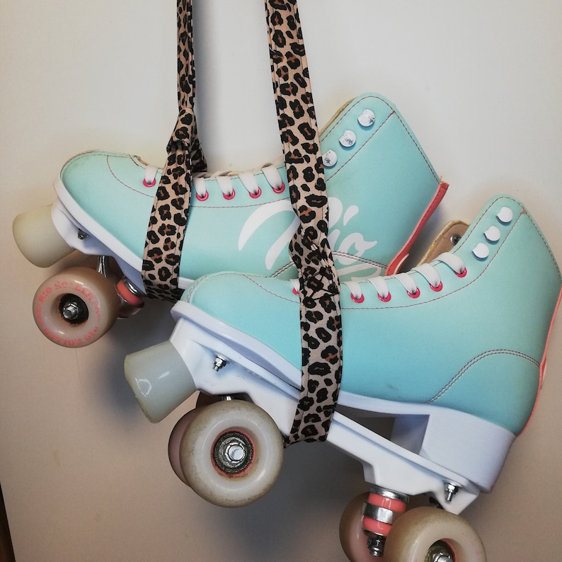 May include: A pair of teal roller skates with pink laces and white wheels. The skates are hanging from a leopard print strap.
