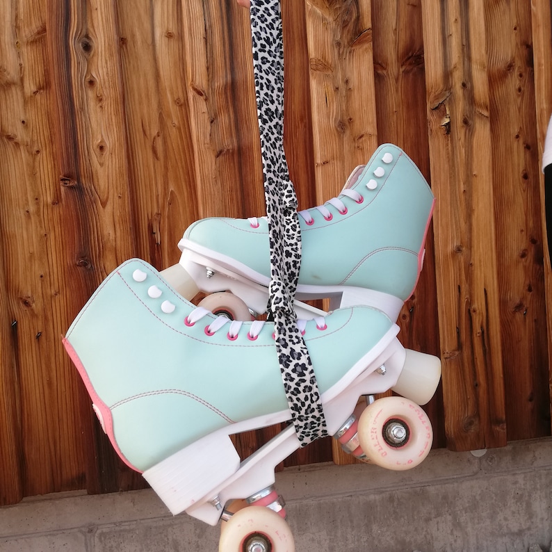 May include: A pair of mint green roller skates with pink laces and white wheels. The skates are connected by a leopard print strap.