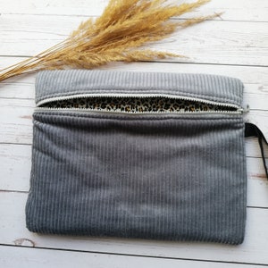 Könnte beinhalten: Eine graue Cord-Zipper-Tasche mit Leopardenmuster-Futter. Die Tasche ist offen und der Reißverschluss ist sichtbar.