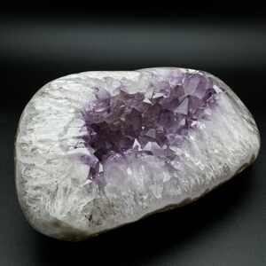 May include: A large amethyst geode with a hollow center filled with purple crystals. The geode is white and translucent with a smooth, rounded exterior.