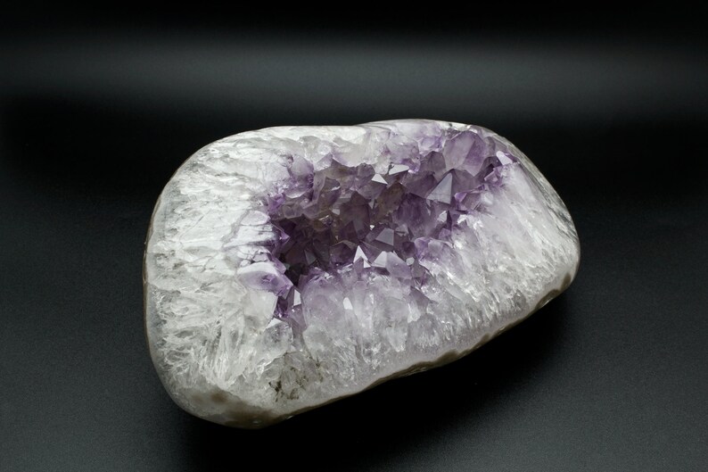 May include: A large amethyst geode with a hollow center filled with purple crystals. The geode is white and translucent with a smooth, rounded exterior.