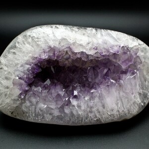 May include: A large, smooth, white agate geode with a hollow center filled with clusters of purple amethyst crystals.