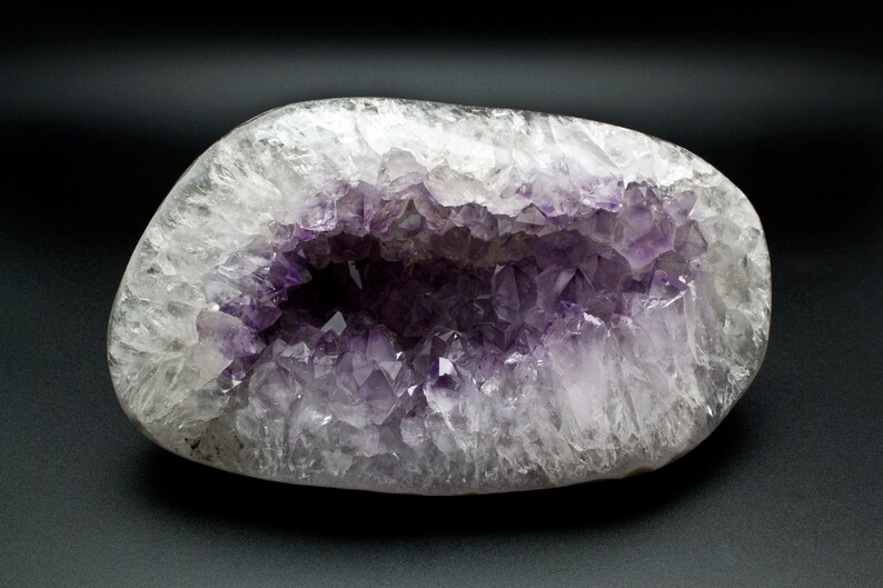 May include: A large, smooth, white agate geode with a hollow center filled with clusters of purple amethyst crystals.