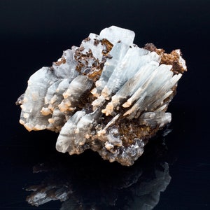 May include: A cluster of light blue barite crystals with a brown matrix. The crystals are elongated and have a glassy appearance. The mineral specimen is displayed against a black background.