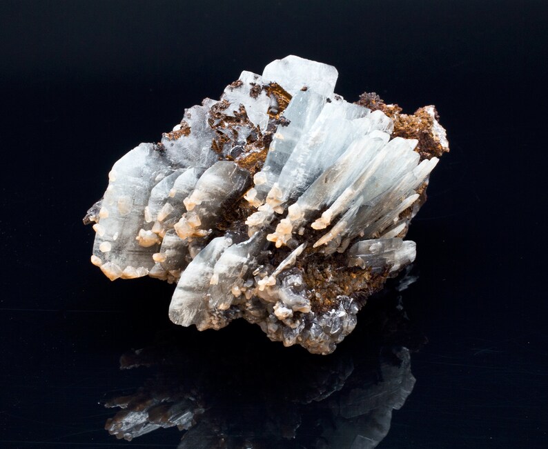 May include: A cluster of light blue barite crystals with a brown matrix. The crystals are elongated and have a glassy appearance. The mineral specimen is displayed against a black background.