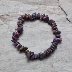 Pode incluir: Um bracelete feito de pequenas pedras de forma irregular em tons de roxo, rosa e azul.
