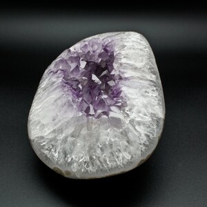 May include: A large, white, and purple amethyst geode with a cluster of crystals in the center. The geode is smooth and polished, with a natural, organic shape.