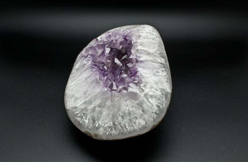 May include: A large, white, and purple amethyst geode with a cluster of crystals in the center. The geode is smooth and polished, with a natural, organic shape.