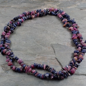 May include: A strand of pink and blue gemstone beads, made of natural, irregular shaped stones. The beads are strung on a clear cord and are approximately 18 inches long.