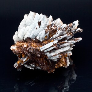 May include: A cluster of white, crystalline formations with a layered structure, interspersed with areas of brown and orange mineral deposits. The mineral specimen is set against a black background, creating a contrast that highlights its natural textures.