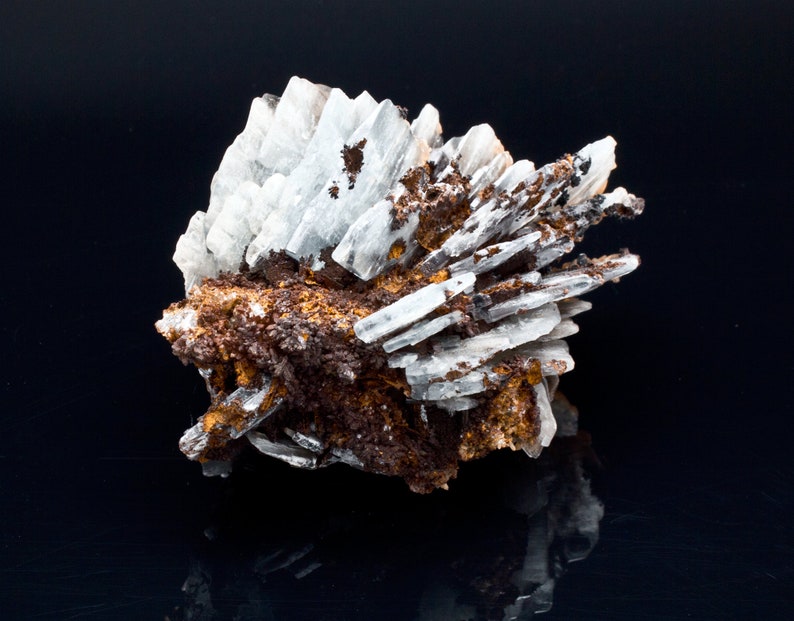 May include: A cluster of white, crystalline formations with a layered structure, interspersed with areas of brown and orange mineral deposits. The mineral specimen is set against a black background, creating a contrast that highlights its natural textures.