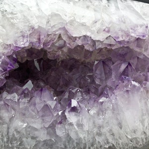 May include: A large amethyst geode with a hollow center lined with purple crystals. The geode is white and translucent, with a smooth, polished surface.