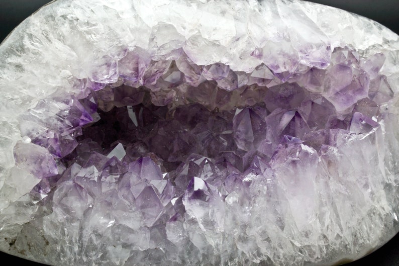 May include: A large amethyst geode with a hollow center lined with purple crystals. The geode is white and translucent, with a smooth, polished surface.