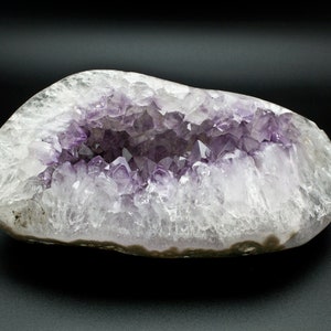 May include: A large, natural amethyst geode with a hollow center lined with purple crystals. The geode is a light gray color with a smooth, rounded exterior.