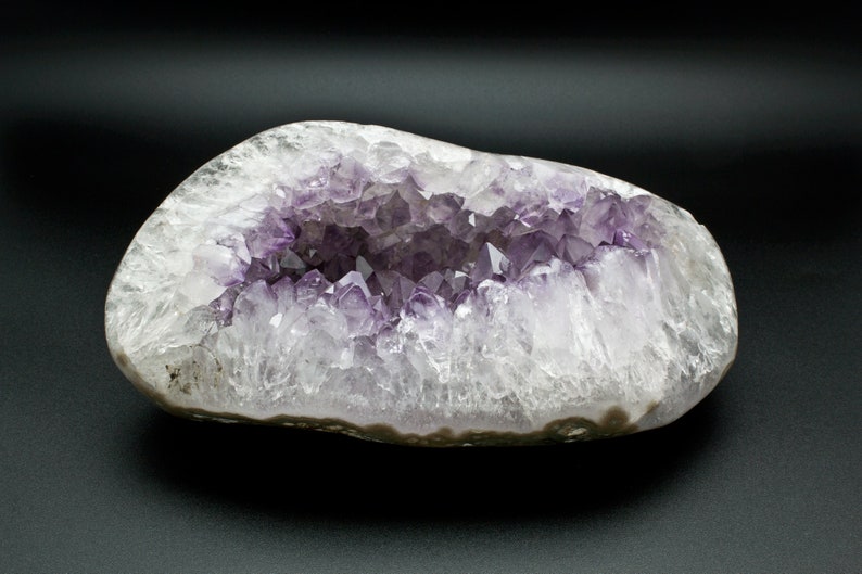 May include: A large, natural amethyst geode with a hollow center lined with purple crystals. The geode is a light gray color with a smooth, rounded exterior.