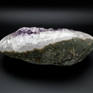 May include: A large, irregularly shaped amethyst geode with a purple crystal cluster inside. The exterior of the geode is a dark gray with a rough texture.