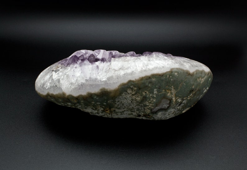 May include: A large, irregularly shaped amethyst geode with a purple crystal cluster inside. The exterior of the geode is a dark gray with a rough texture.