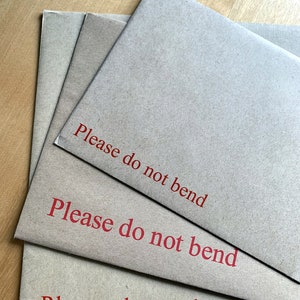 Op de afbeelding: Drie bruine enveloppen gestapeld op elkaar. De bovenste envelop heeft de tekst "Please do not bend" in het rood gedrukt. De middelste envelop heeft dezelfde tekst in het rood gedrukt. De onderste envelop heeft dezelfde tekst in het rood gedrukt.